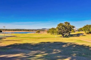 Um campo de golfe com um corpo d'água, árvores e um céu claro.