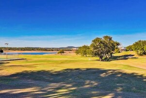 Um campo de golfe com um corpo d'água, árvores e um céu claro.