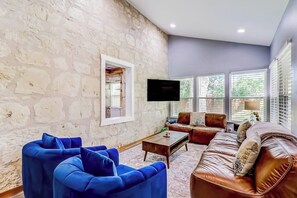 Ein Wohnzimmer mit einer Steinwand, einem Fernseher, einem braunen Ledersofa und einem blauen Sessel.