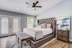 Ein Schlafzimmer mit einem großen Bett, einem Deckenventilator, einer Bank und einem Nachttisch mit Lampe.