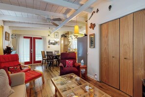 Uma sala de estar com mesa de centro de vidro, poltronas vermelhas, piso de madeira, ventilador de teto e guarda-roupa de madeira.