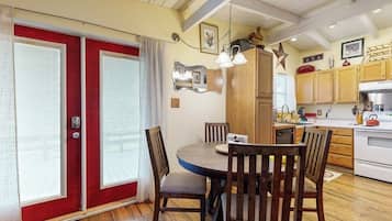 A dining area with a round table, wooden chairs, a red door, and a kitchen with wooden cabinets and a white stove.