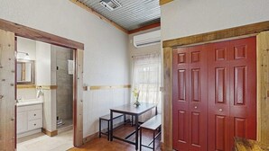 Una habitación con piso de madera, un escritorio con silla, una puerta roja y una ventana con cortinas.