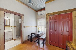 A room with a wooden floor, a desk with a chair, a red door, and a window with curtains. - Romantic, Dog-friendly Cabin With On-site Courtyard, Close to Wineries (Fredericksburg)