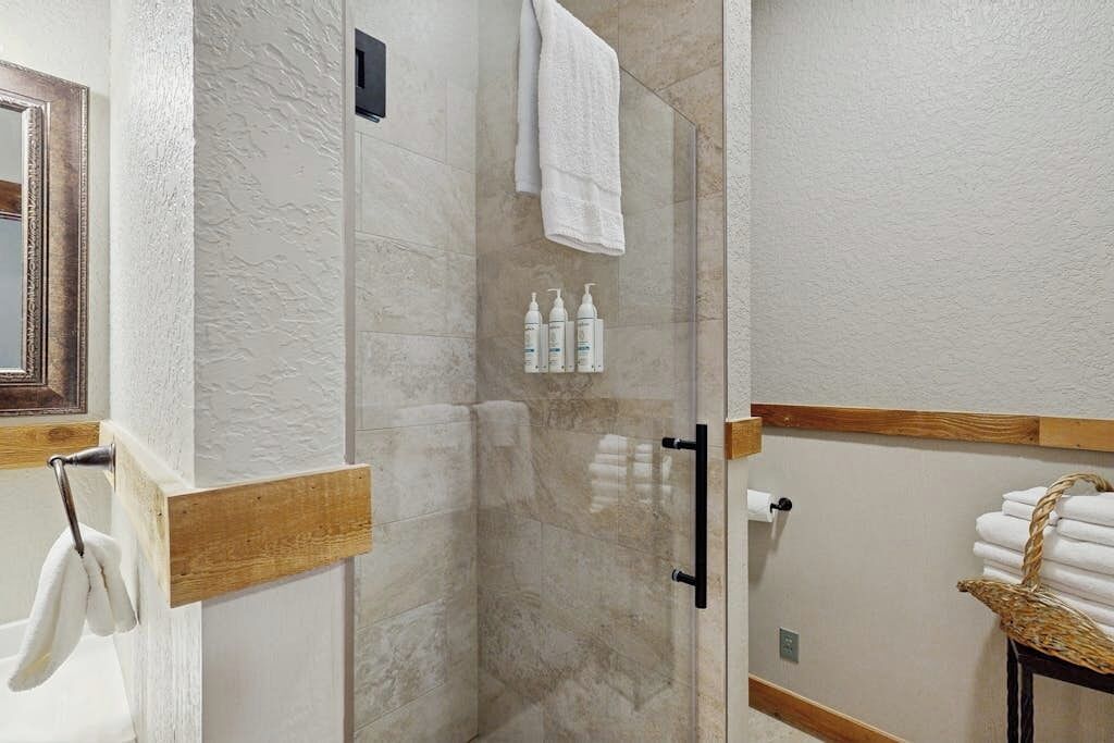 A bathroom with a glass shower enclosure, a wooden towel rack, and a basket of towels.
