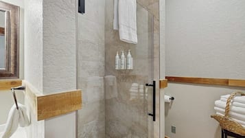 A bathroom with a glass shower enclosure, a wooden towel rack, and a basket of towels.