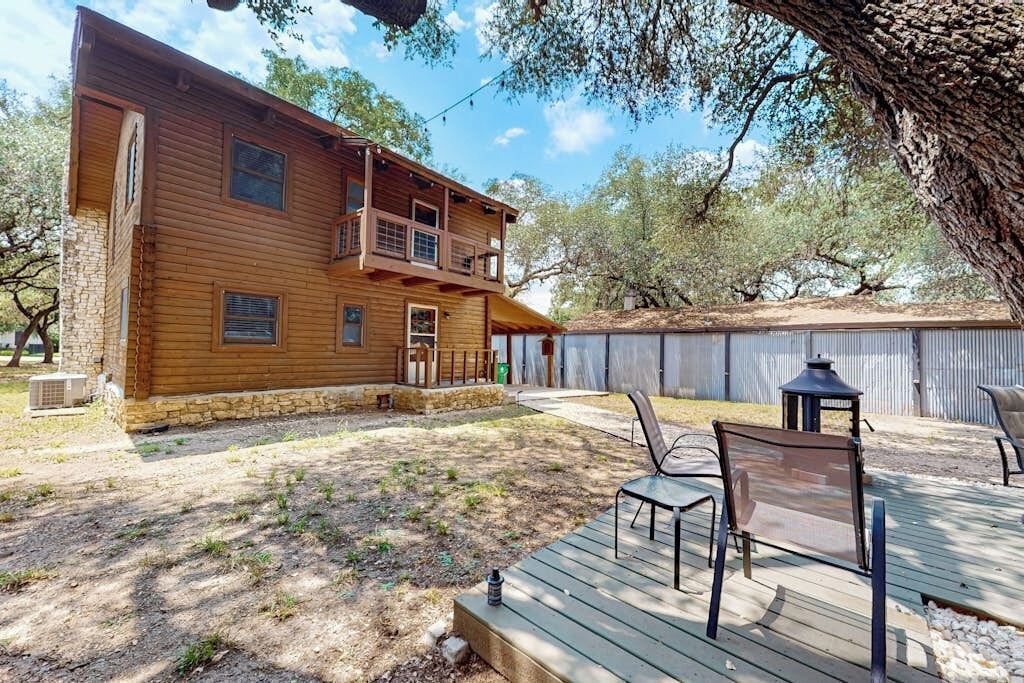 A wooden house with a balcony, a patio with chairs, and a tree in the background.