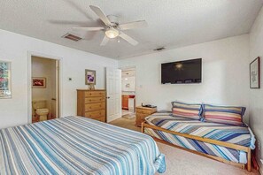 Quarto com duas camas, ventilador de teto, televisão e porta para um banheiro.