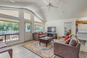 Uma sala de estar ampla com uma televisão grande, assentos confortáveis e vista através das portas de vidro.
