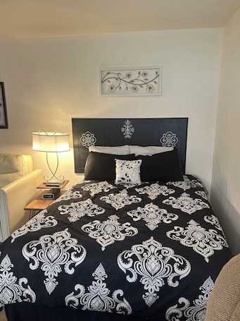 A neatly made bed with a black and white patterned bedspread, a bedside lamp, a clock, and a framed floral artwork on the wall.. Cozy, Fully Furnished, Apartment near Mark Twain Lake -Sleeps 4-Boat Parking