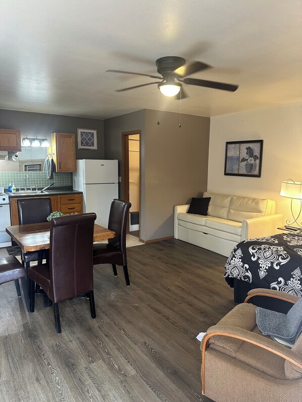 Un espacio habitable compacto con comedor, kitchenette y zona de estar con sofá y sillón.