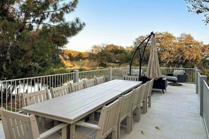 An outdoor patio with a long table and chairs, surrounded by a white railing, overlooking a natural landscape. - Waterfront, Dog-friendly Home With Lake Views, Private Boat Lift & Dock (Horseshoe Bay)