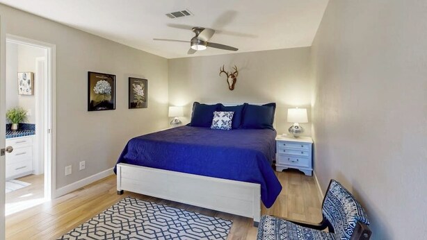 A bedroom with a bed, nightstands, a ceiling fan, and wall-mounted artwork. - Waterfront, Dog-friendly Home With Lake Views, Private Boat Lift & Dock (Horseshoe Bay)