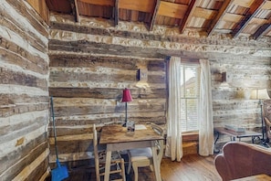 Ein rustikales Blockhaus-Interieur mit einem Holztisch, Stühlen, einer Lampe und einem Fenster mit Vorhängen.