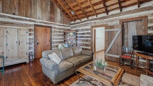 A rustic interior with wooden walls, a sofa, a coffee table, and a television. - Five Dog-friendly Suites on Hwy 290 Wine Trail (Fredericksburg)