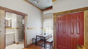 A room with a wooden floor, a desk with a chair, a red door, and a white wall with a window. - Five Dog-friendly Suites on Hwy 290 Wine Trail (Fredericksburg)