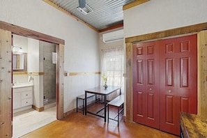 Ein Zimmer mit Holzboden, einem Schreibtisch mit Stuhl, einer roten Tür und einer weißen Wand mit Fenster.
