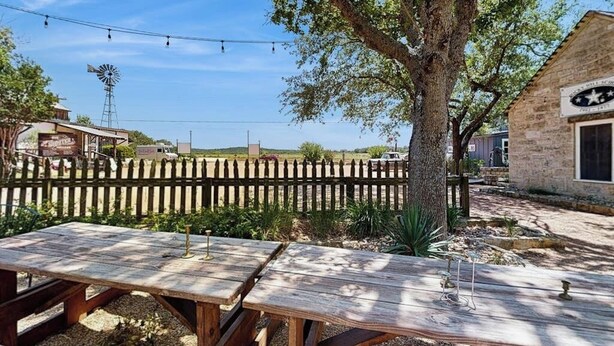 A rustic outdoor seating area with picnic tables, a wooden fence, and a windmill in the background. - Five Dog-friendly Suites on Hwy 290 Wine Trail (Fredericksburg)