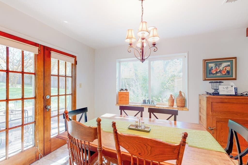 Un coin repas avec une table en bois, des chaises, un lustre et une fenêtre donnant sur un paysage verdoyant.