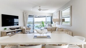 Een moderne woonkamer met een grote flatscreen televisie, een witte eettafel en een bank.