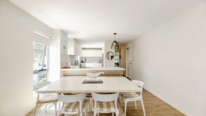 A modern kitchen with white cabinetry, a central island, and a dining area with a white table and chairs. - 9 'Noosa Moorings' 303 Gympie Terrace Noosaville (Noosaville)