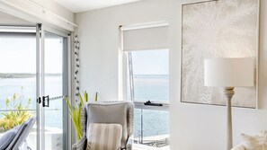 Een kamer met uitzicht op zee, een stoel, een lamp en een lijst met een kunstwerk.