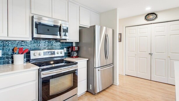 A modern kitchen with stainless steel appliances, white cabinetry, and a blue backsplash. - Peaceful, Modern Home Close to Lago Vista With Large Deck & Balcony (Marble Falls)