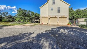 A two-story house with a garage, surrounded by a gravel driveway and trees. - Peaceful, Modern Home Close to Lago Vista With Large Deck & Balcony (Marble Falls)