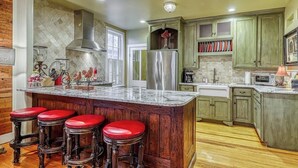 A kitchen with a central island, wooden bar stools, a stainless steel refrigerator, and green cabinetry. - Three Lovely Homes, Group- Family-friendly, Near Downtown, 2 Dogs OK (Fredericksburg)