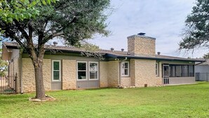 A single-story house with a stone facade, a chimney, and a small front yard. - Peaceful Mid-century Escape With Screened Porch & Lake Access (Leander)