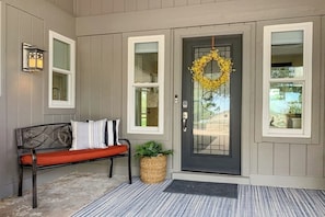 A front porch with a bench, a door with a wreath, and a wall-mounted lantern. - Peaceful Mid-century Escape With Screened Porch & Lake Access (Leander)