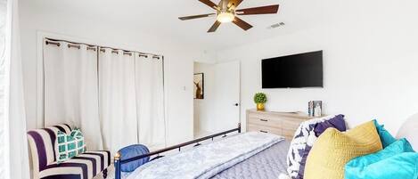 Une chambre à coucher avec un lit, un ventilateur de plafond, une télévision, une chaise et une commode.