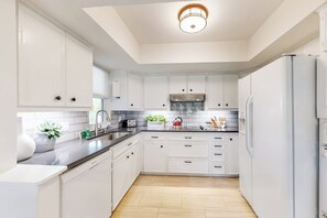 A modern kitchen with white cabinets, a stainless steel sink, and a built-in oven. - Peaceful Mid-century Escape With Screened Porch & Lake Access (Leander)