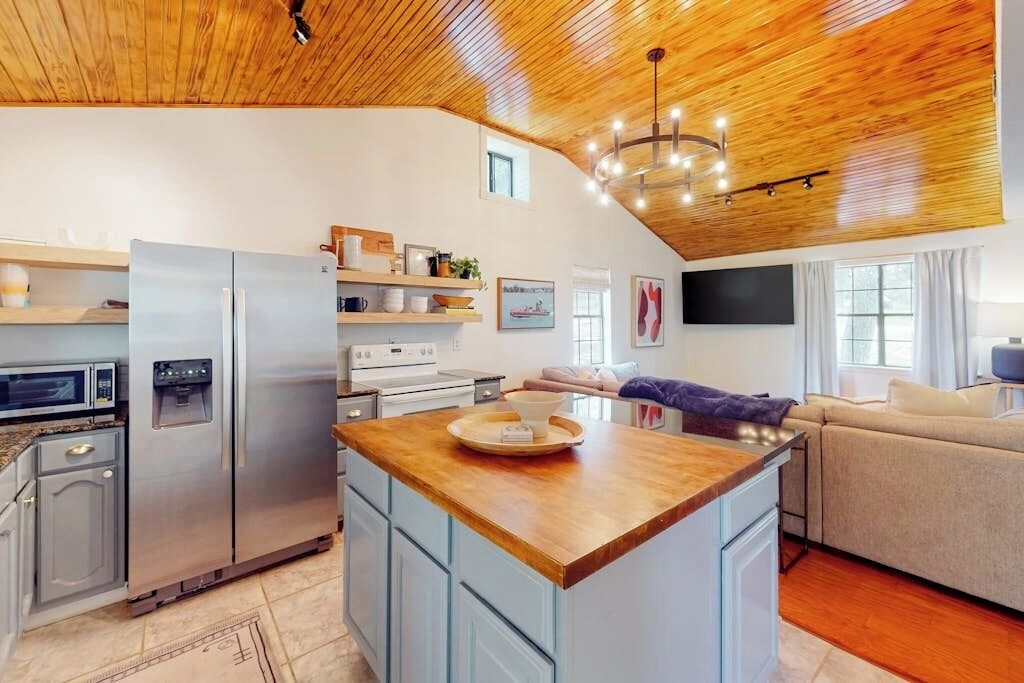 A modern kitchen with a central island, built-in appliances, and a wooden ceiling.
