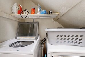 Un área de lavandería con lavadora, secadora y un estante con productos de limpieza.