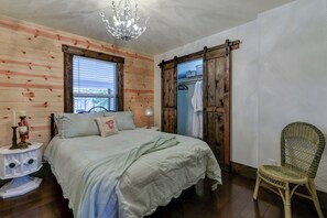 A bedroom with a bed, wooden walls, a chandelier, a chair, and a wardrobe.