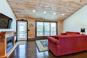 A wooden-paneled room with a fireplace, a red sofa, and a large window.