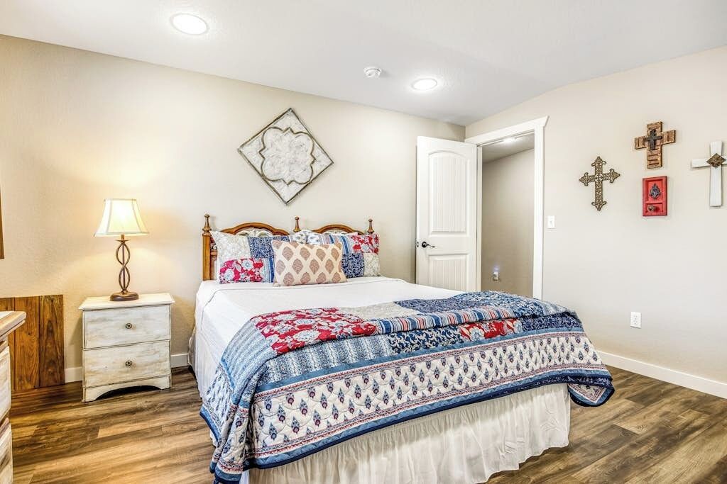 A bedroom with a bed, bedside table, lamp, and wall decorations including a door and crosses.