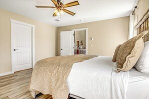 Quarto com cama, ventoinha no teto e uma porta.
