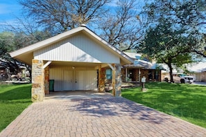 A building with a covered garage, stone pillars, and a brick pathway leading to the entrance. - Cozy Dog-friendly Home With Full Kitchen, Patio & Backyard, Close to Golf Course (Horseshoe Bay)