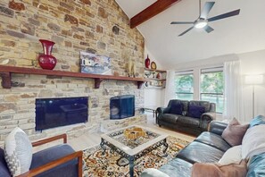 Ein Wohnzimmer mit Steinwand, Kamin, Fernseher, Sofa und Deckenventilator.
