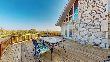 A wooden deck with a table and chairs, stone wall, and a view of the landscape.