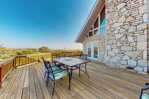 A wooden deck with a table and chairs, stone wall, and a view of the landscape. - Lovely 2-story Home With Upper & Lower Decks, Gorgeous Lake & Hill Country Views (Buchanan Dam)