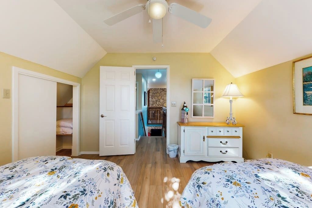 Un dormitorio con dos camas, un ventilador de techo, un aparador y una puerta que da a un pasillo.
