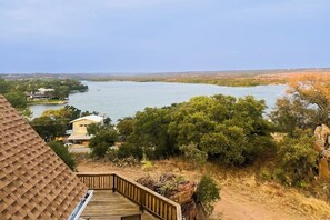 A wooden deck overlooking a lake with surrounding trees and a distant view of houses. - Lovely 2-story Home With Upper & Lower Decks, Gorgeous Lake & Hill Country Views (Buchanan Dam)