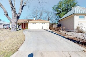 A residential house with a driveway, a garage, and a tree in the yard. - Cozy & Cute Cabin With Fenced Patio, Grill, AC & Wifi - Walkable Locale (Fredericksburg)