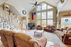 Un salon spacieux avec une grande fenêtre, un escalier orné de croix fixées au mur et un drapeau du Texas.