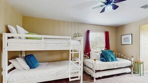 A bunk bed room with a ceiling fan, a window with curtains, and a framed picture on the wall.