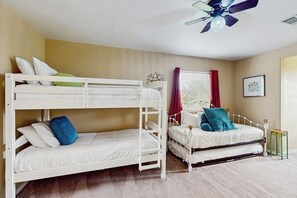 A bunk bed room with a ceiling fan, a window with curtains, and a framed picture on the wall.