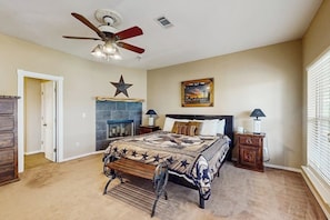 A bedroom with a bed, a ceiling fan, a fireplace, a star decoration, and a nightstand with a lamp.
